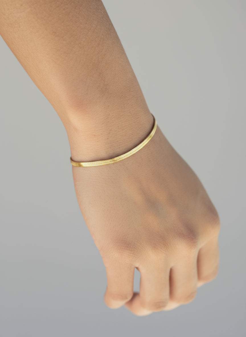 Gold beachwear bracelet on a person's ankle with a blurred beach background