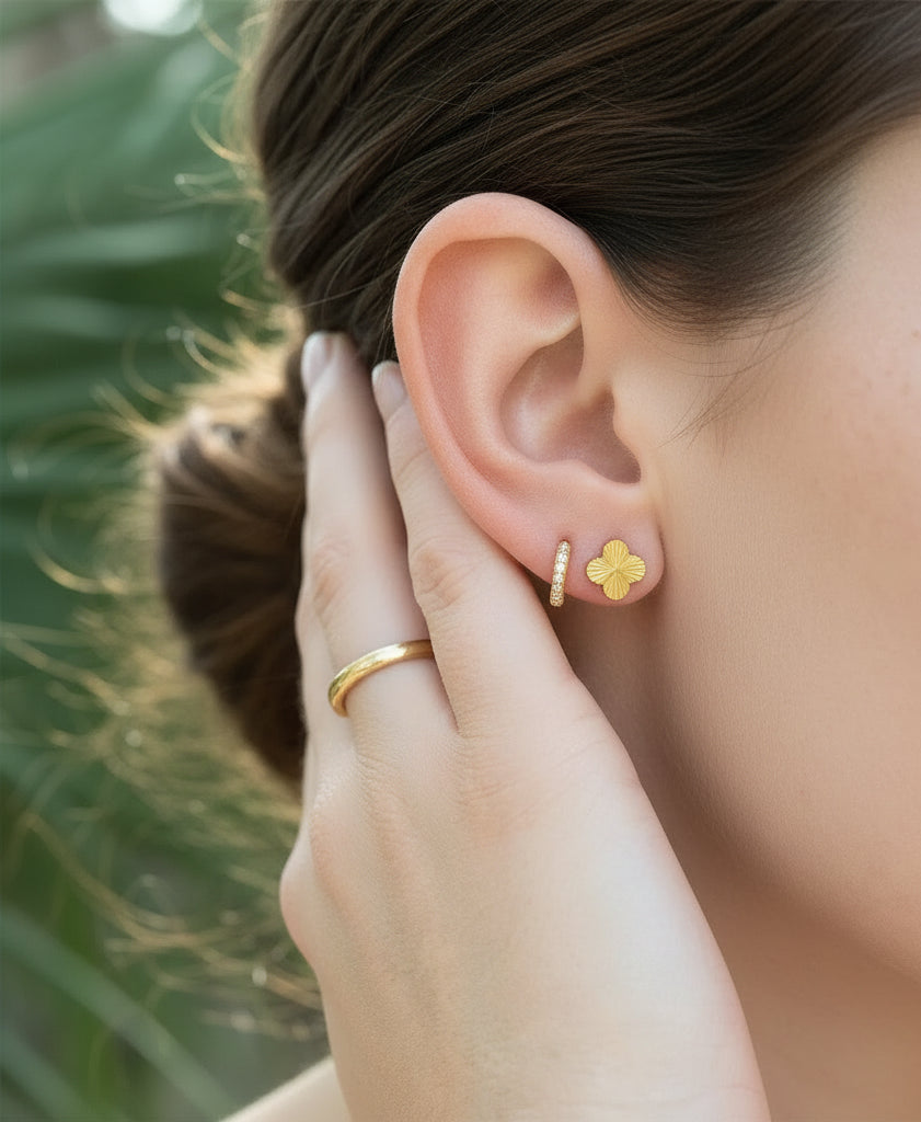 Close-up of a person wearing gold earrings with a blurred green background