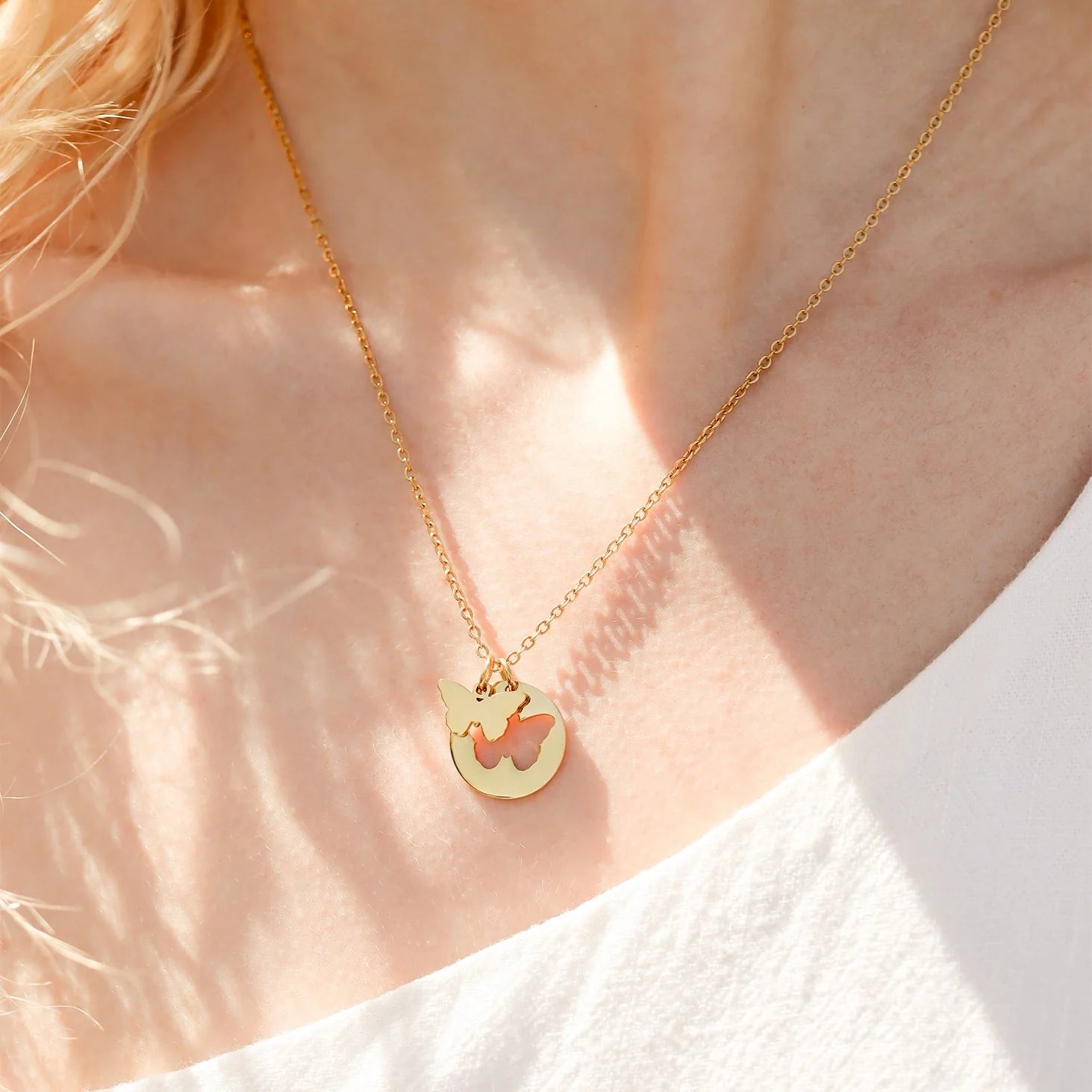 Gold necklace with a heart-shaped pendant on a person wearing a white shirt.
