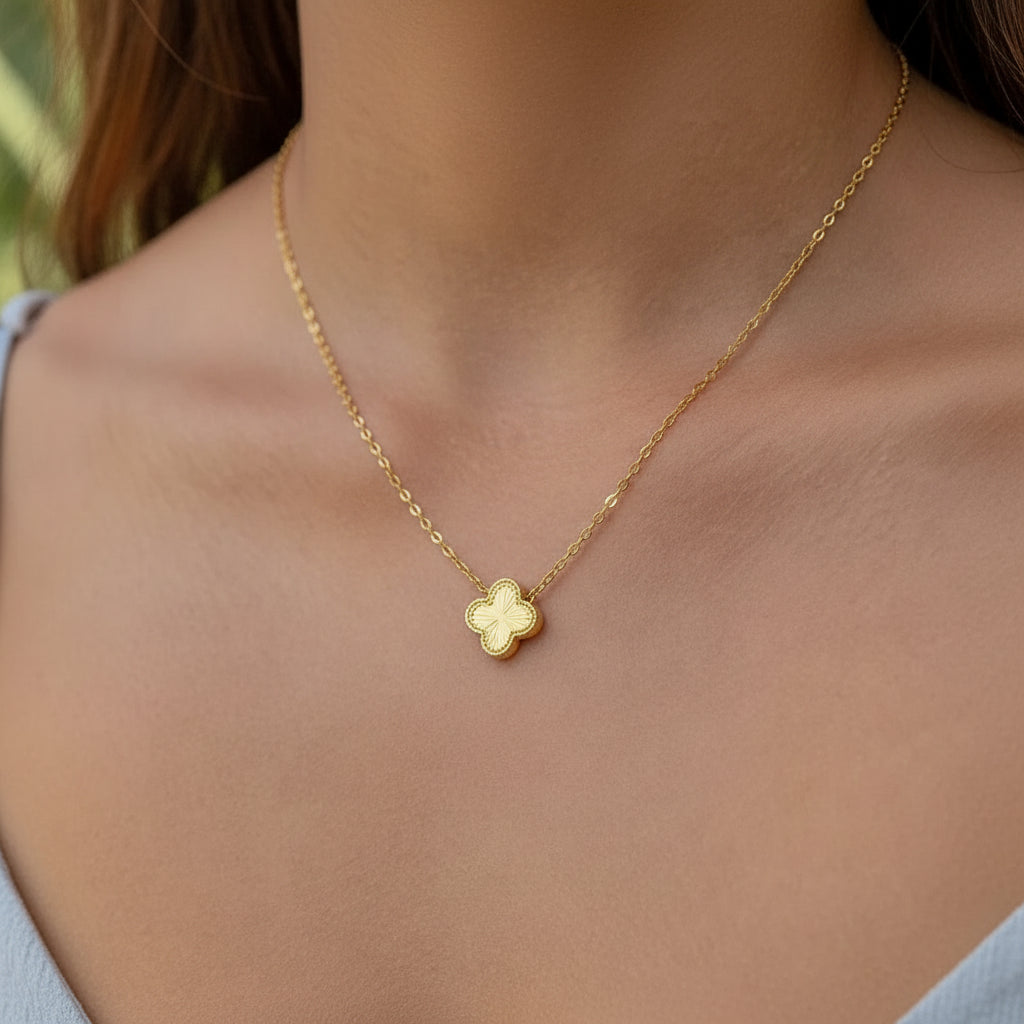 Gold pendant in a clover necklace on a person's neck against a blurred natural background