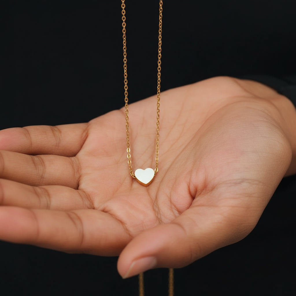 Gold necklace with a heart pendant held in a hand against a black background