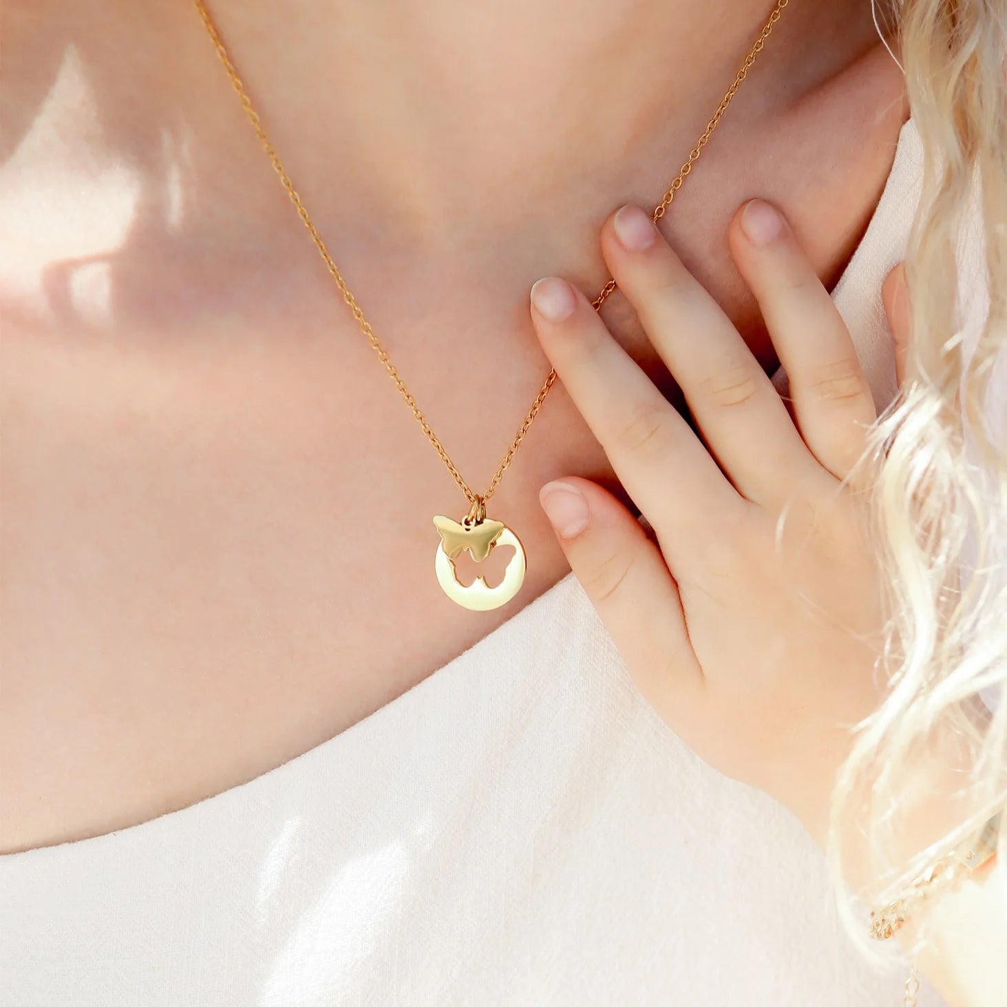 Gold necklace with a butterfly pendant worn by a person, with a hand touching the neck.