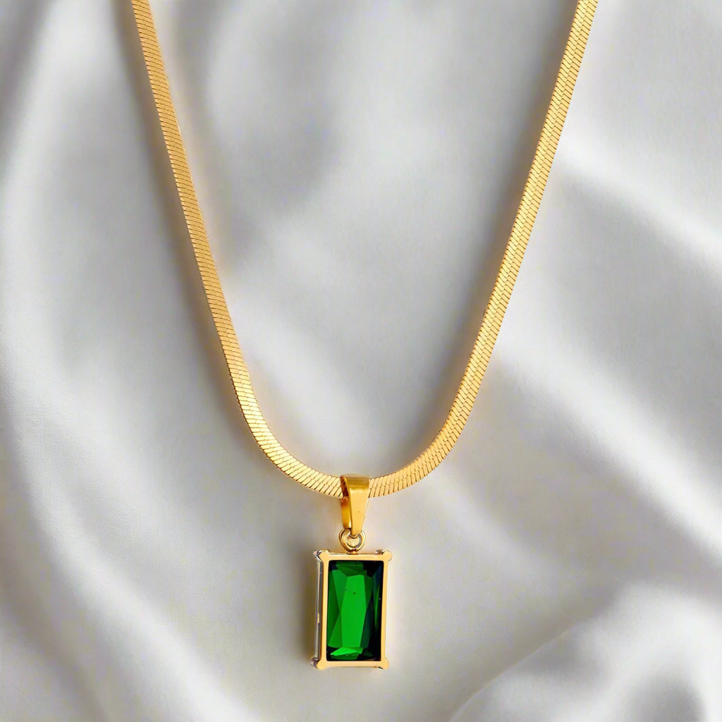Gold necklace with a green emerald pendant on a white background
