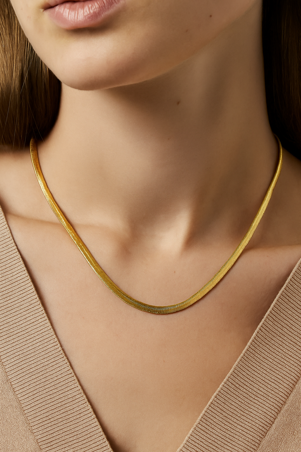 Gold necklace worn by a person with a neutral background