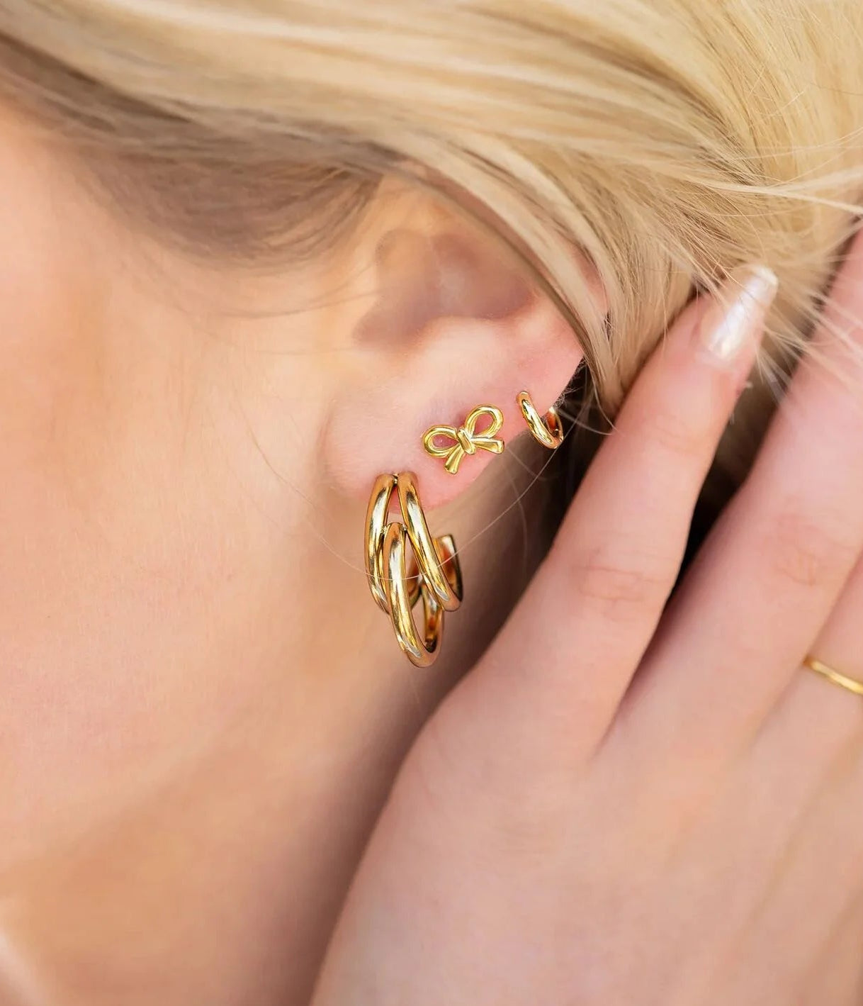 Close-up of a person wearing gold hoop huggie earrings with a hand adjusting them.