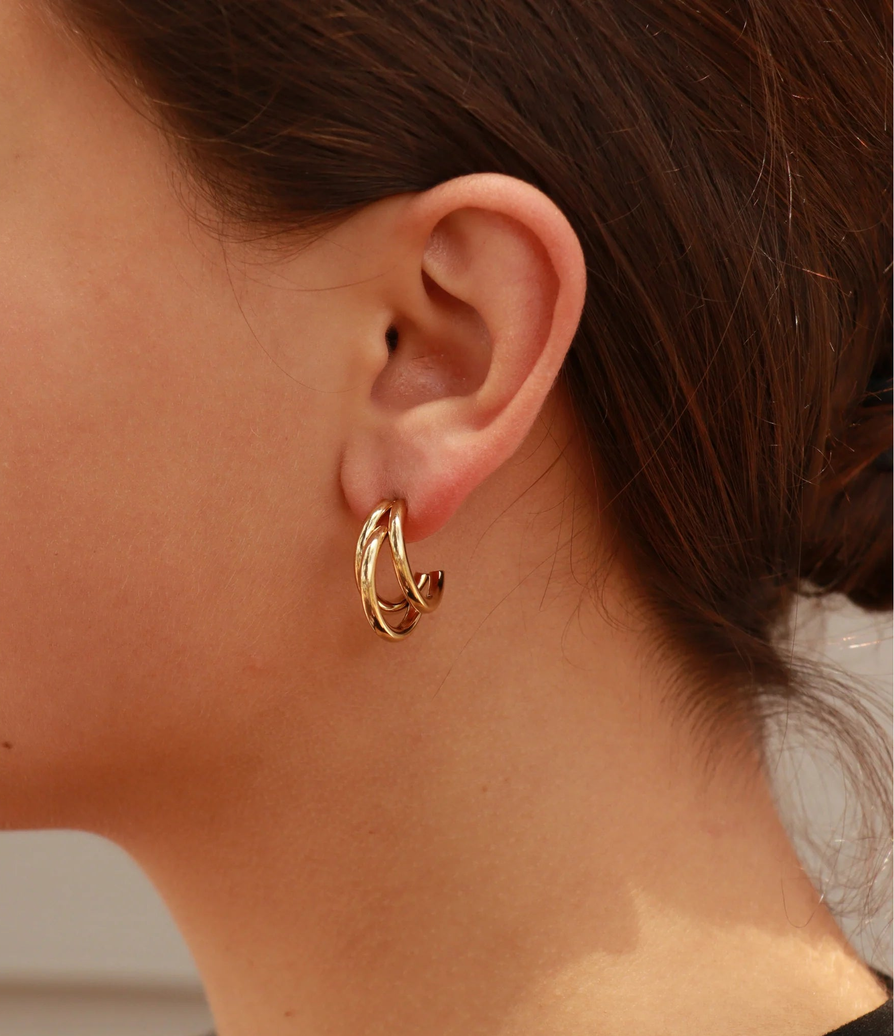 Close-up of a person wearing a gold huggie earrings with a neutral background