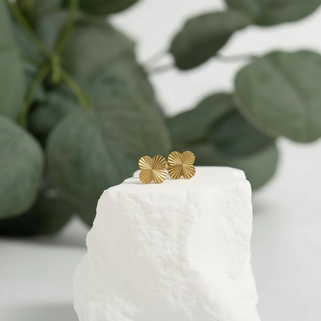 Gold earrings on a white pedestal with green leaves in the background