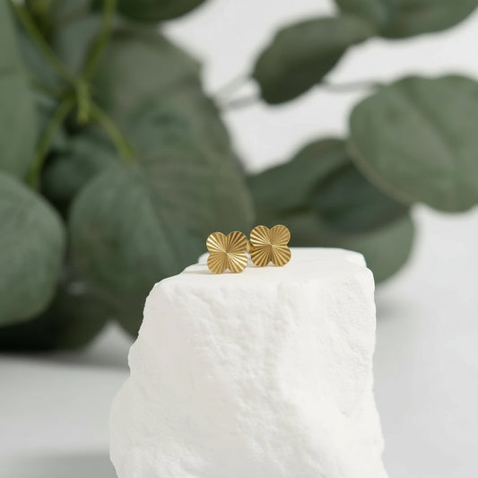 Gold earrings on a white pedestal with green leaves in the background