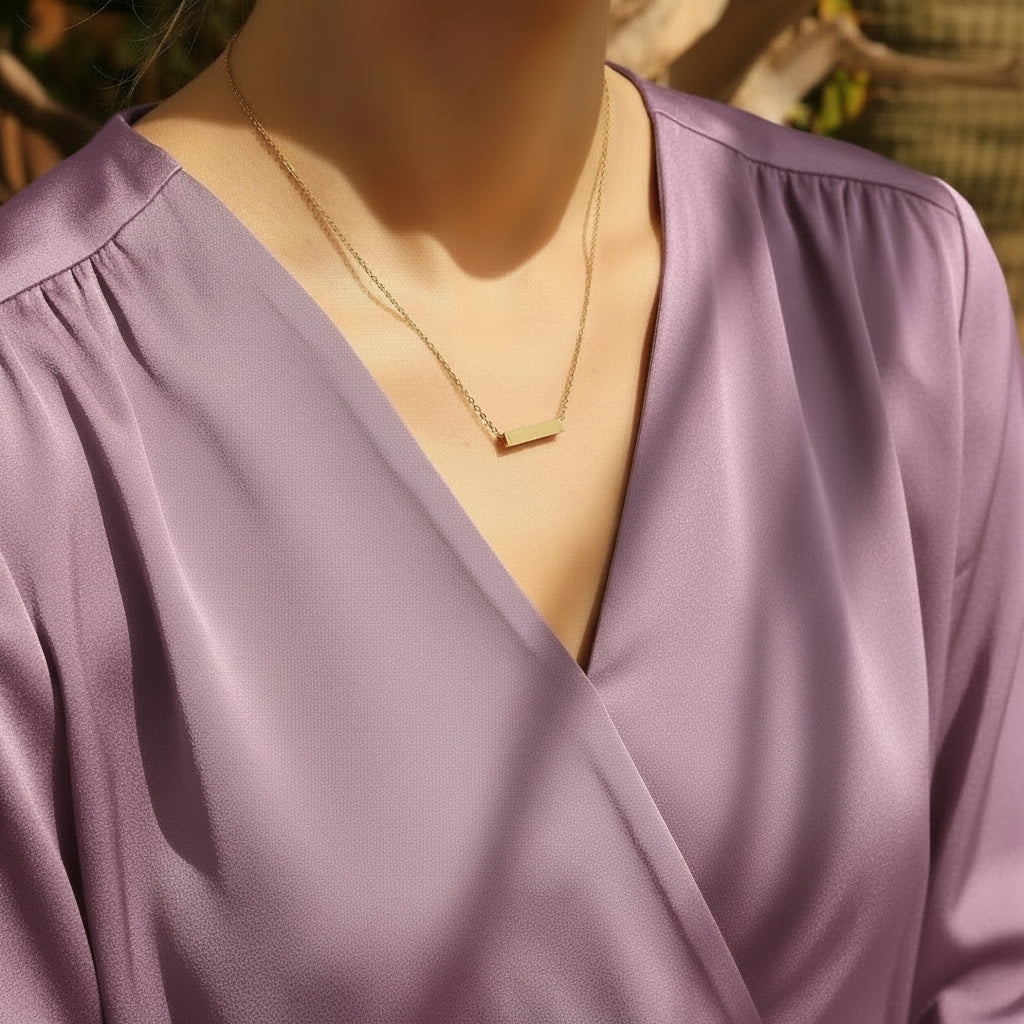 Gold necklace with a bar pendant worn by a person in a white top.