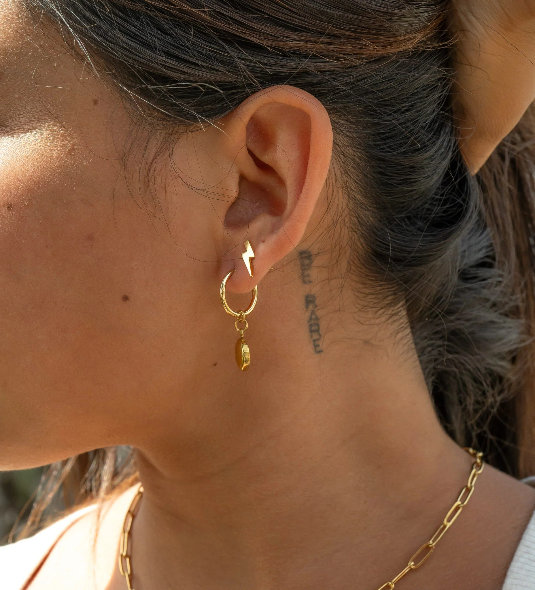 Close-up of a person wearing gold hoop earrings with a blurred natural background