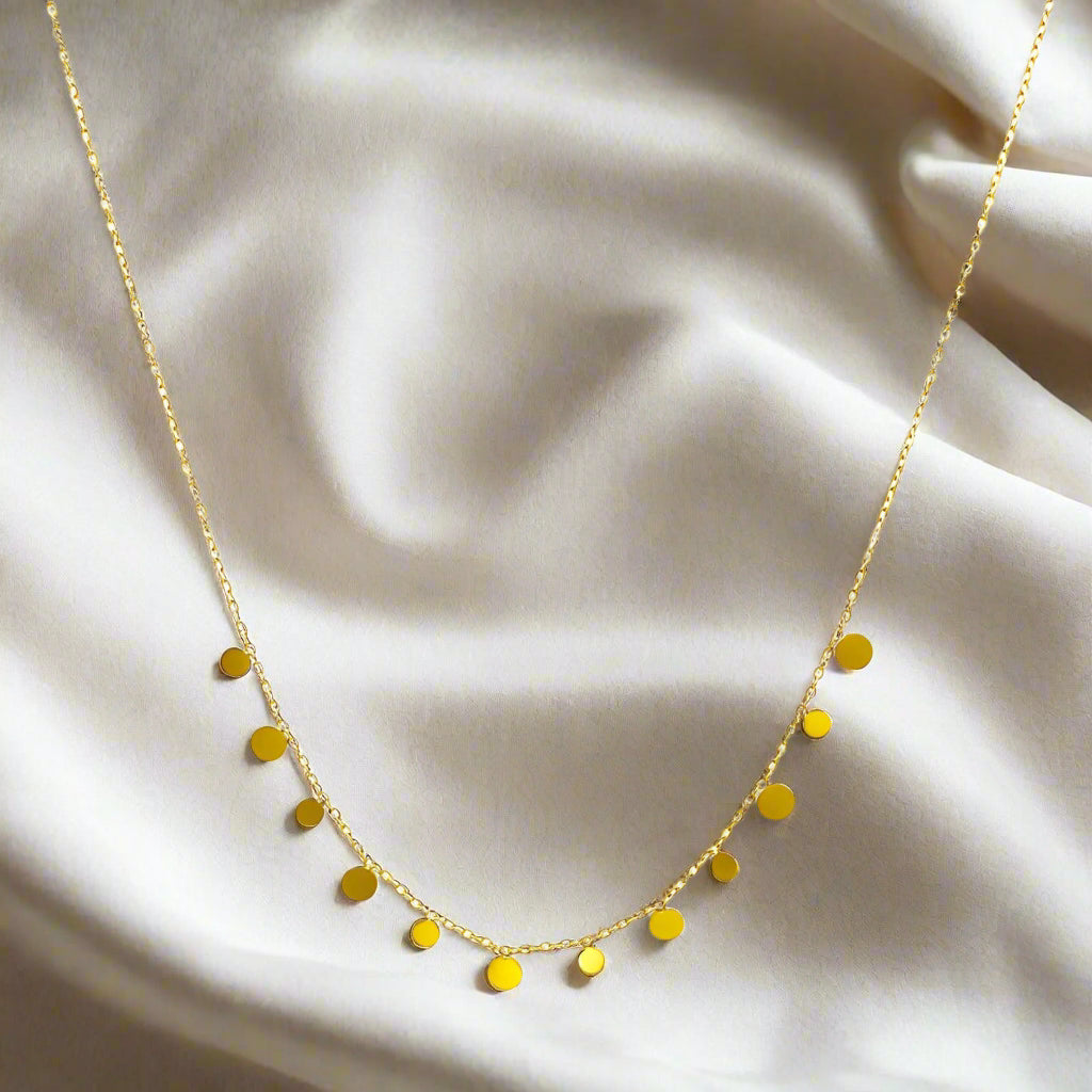 Gold plated necklace with small round pendants on a nude background